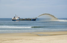 This stock image shows a ship spouting sand in front of the coast to gain new land from the sea.
