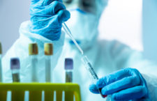 Close up photo of female scientist holding a laboratory pipette and a blood sample tube for covid-19 in laboratory. She is wearing a protective suit, laboratory glasses, surgical mask and surgical gloves. Selective focus on tube. Shot with a full frame mirrorless camera.