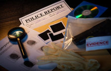 Fictious police desk with crime case records containing gun, blank photos, crime scene information sheet, cd rom, magnifying glass, gloves and police reports.